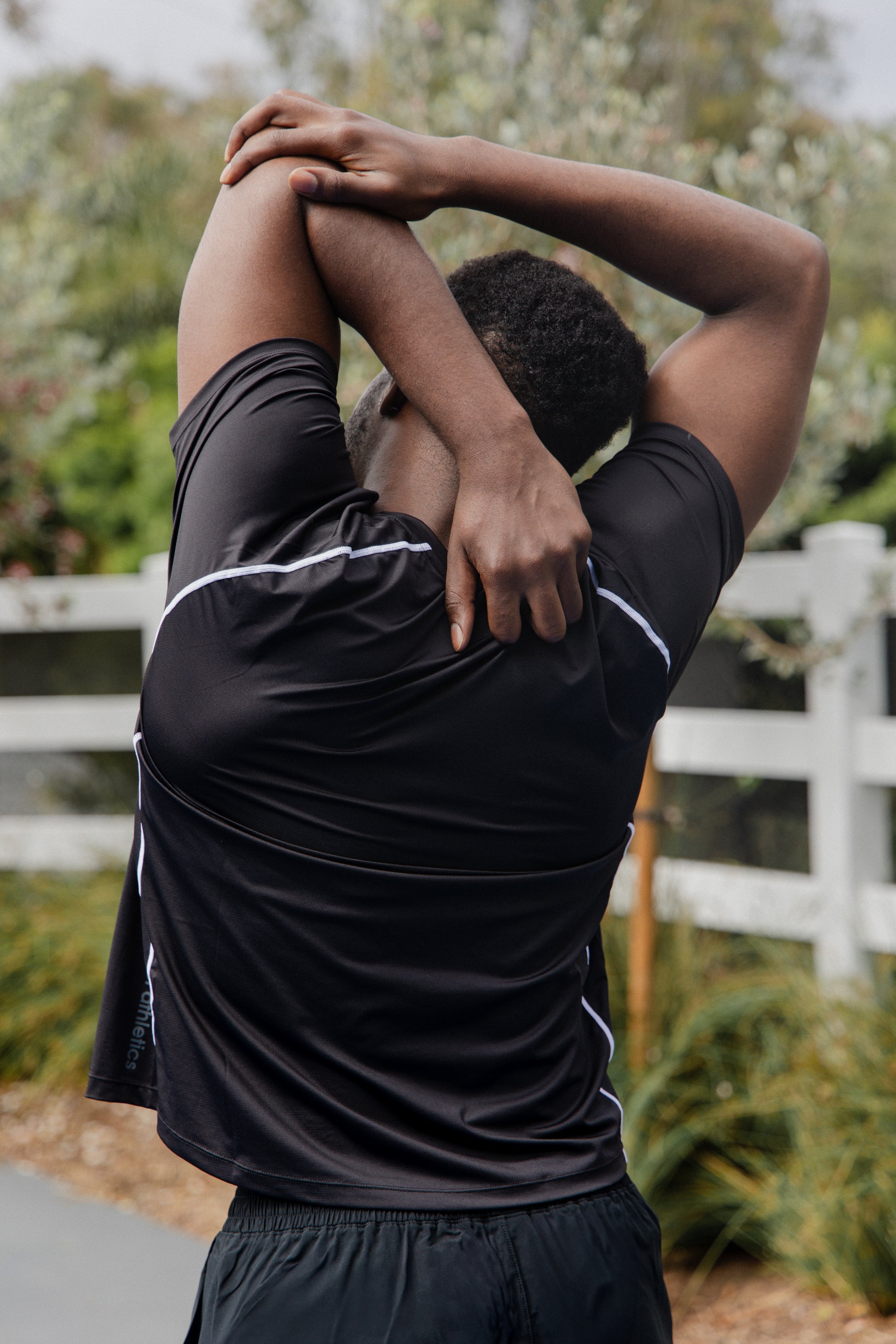 male pickleball player wearing black unlined athletic shorts and a black athletic shirt stretching